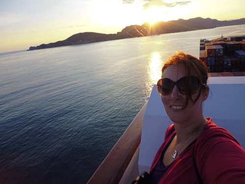 Rebecca Hall on deck at sunset, with the Greek coastline behind her